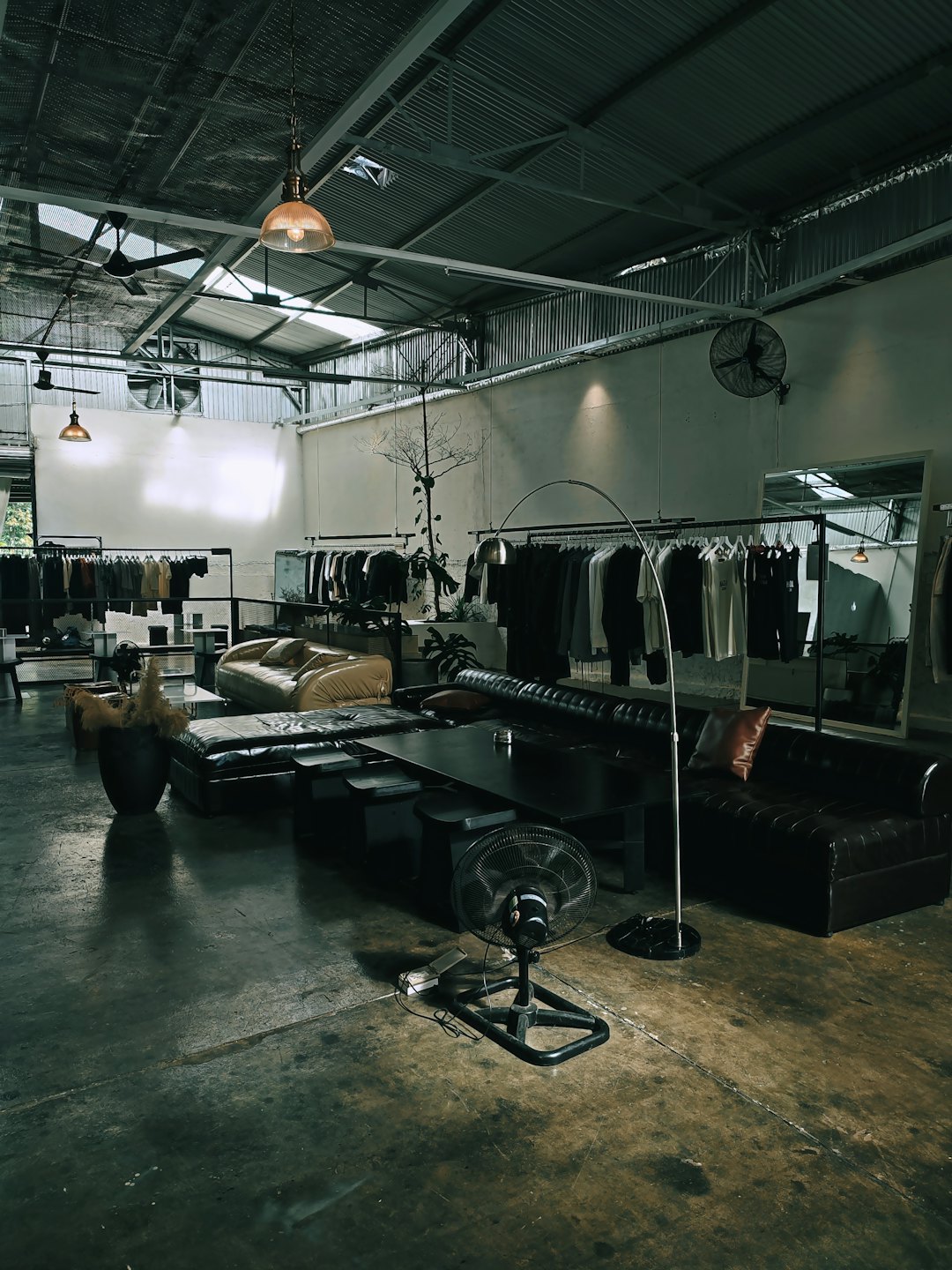 Moderne Boutique mit Kleiderständern und Ledersitzen auf Betonboden.